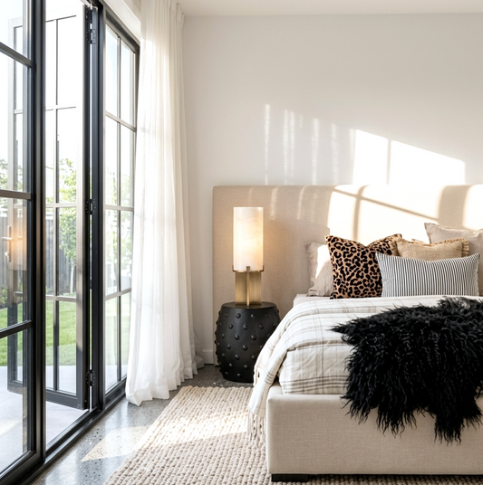 Atelier Noir black studded side table styled in a warm bedroom beside a bed with dark linen and a pendant lamp