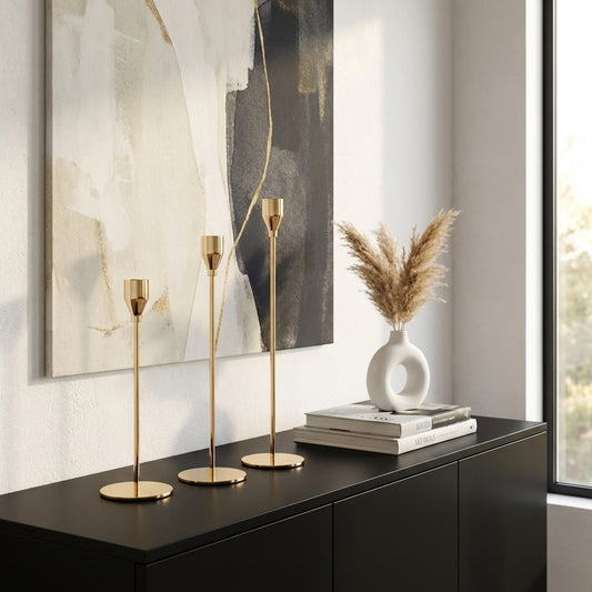 Decorative setup with gold candle holders, a white vase with dried plants, and books on a black surface.