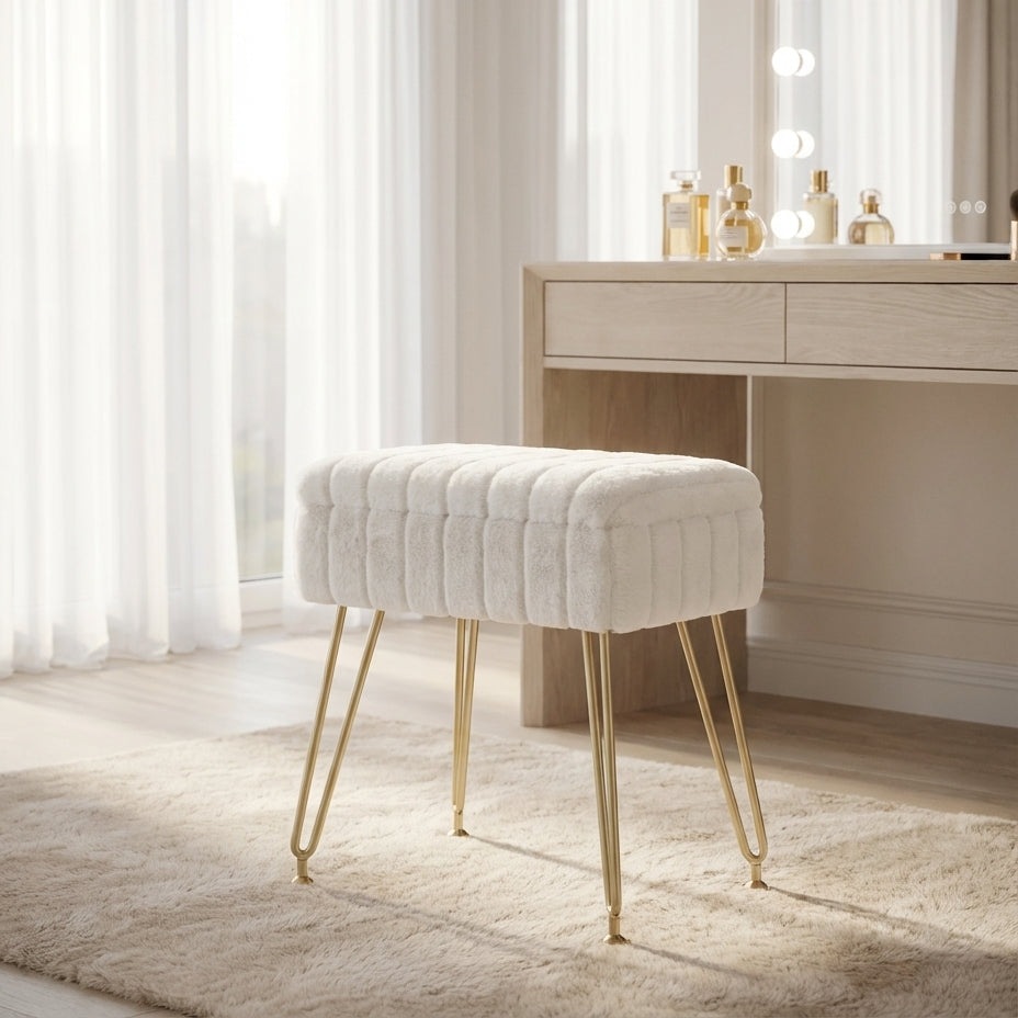 White tufted stool with gold legs in front of a vanity table with lights.
