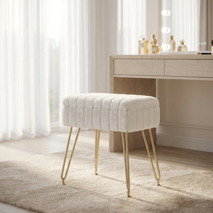 White tufted stool with gold legs in front of a vanity table with lights.