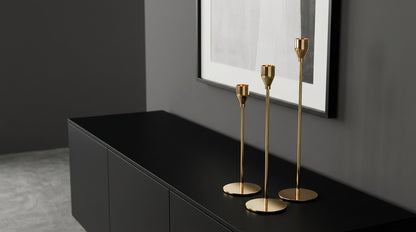 Gold candle holders on a black surface with a gray wall and framed picture in the background
