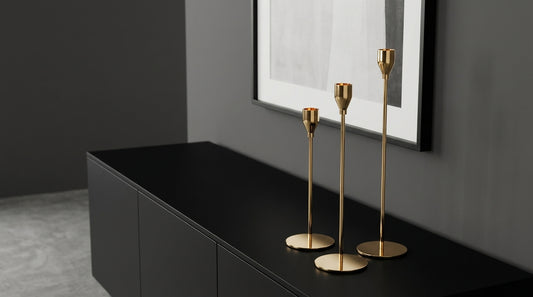 Gold candle holders on a black surface with a gray wall and framed picture in the background