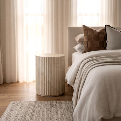 Vera fluted stone side table styled in a warm bedroom setting with white linen and soft natural tones