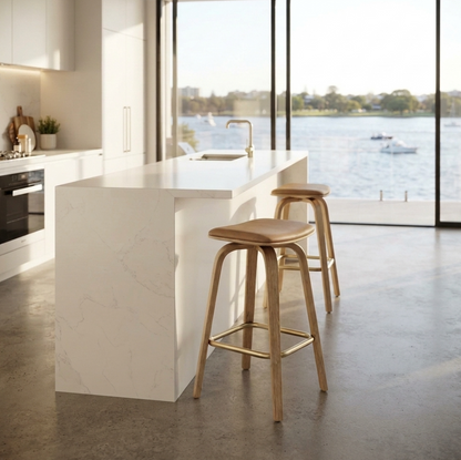 Remi backless swivel bar stool set of two in tan leather with bentwood oak frame and gold footrest ring, styled at a marble kitchen island with water views